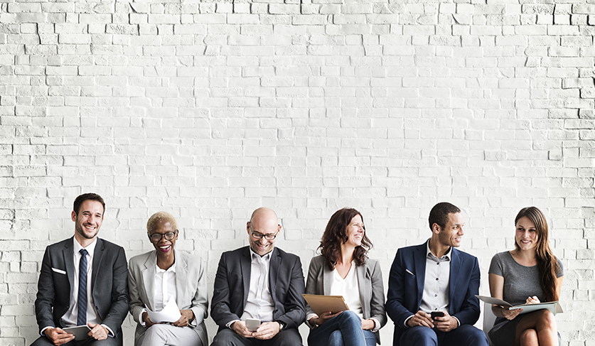 six people in suits seating in front of a white brick wall