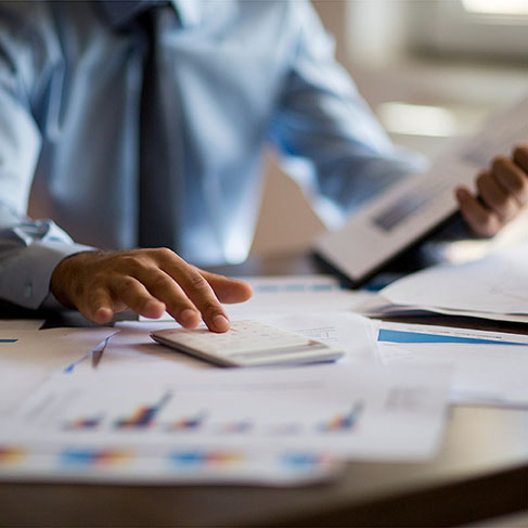 Business man using calculator on desk covered in graph papers in office