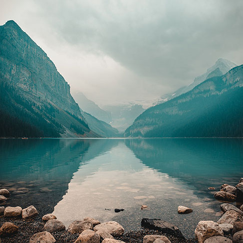 Rocky lake shore with mountains in the background during cloudy day